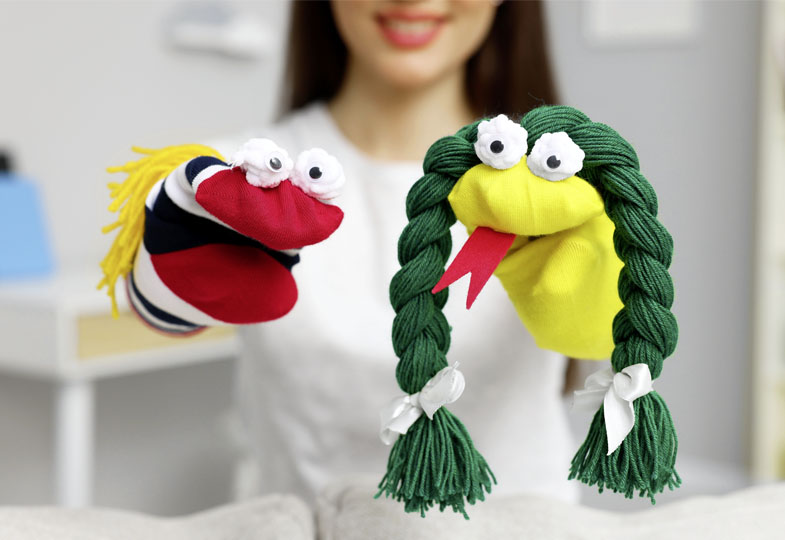 Zwei Handpuppen mit großen Augen: Eine ist gelb mit zwei grünen Zöpfen, die andere hat einen roten Mund, gelbe Haare und einen schwarz-weiß gestreiften Körper.