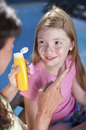 Ein Kind, dem gerade Sonnencreme sorgfältig ins Gesicht aufgetragen wird.