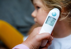 Ein Kind, dem ein digitales Fieberthermometer ans Ohr gehalten wird, das 39 Grad anzeigt.