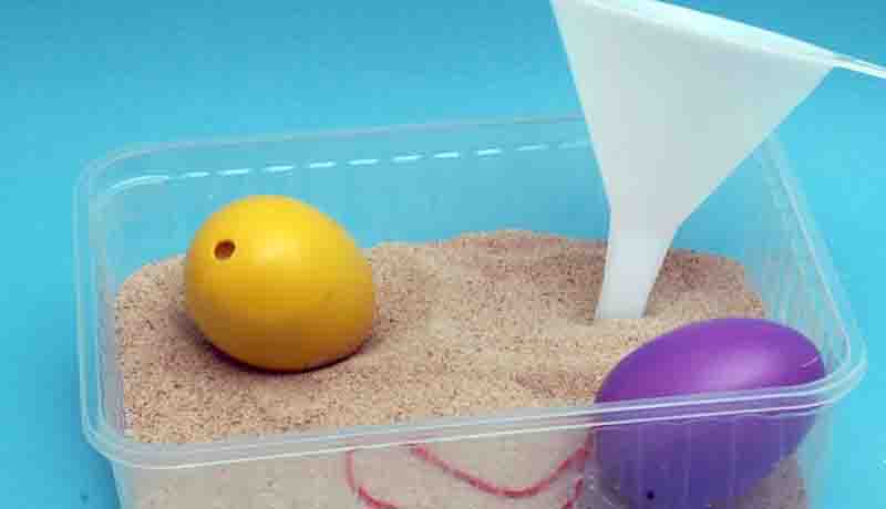 In einer Schale befindet sich Sand, zwei Ostereier und ein Trichter.