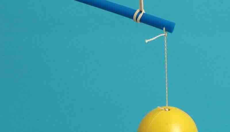 An einem Trinkhalm ist mit einer Schnur ein gelbes Osterei befestigt.