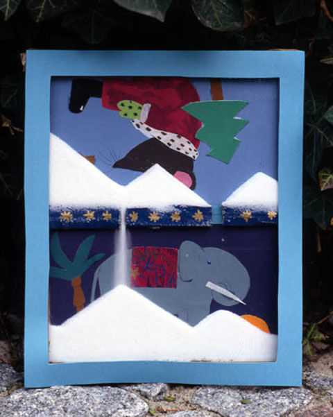 In einem Bilderrahmen befindet sich ein Rieselbild mit Salz. Unten ein Elefant, oben eine Maus mit Tannenbaum.