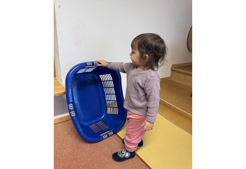 Das Mädchen Josi hält einen blauen Wäschekorb in einer Hand.
