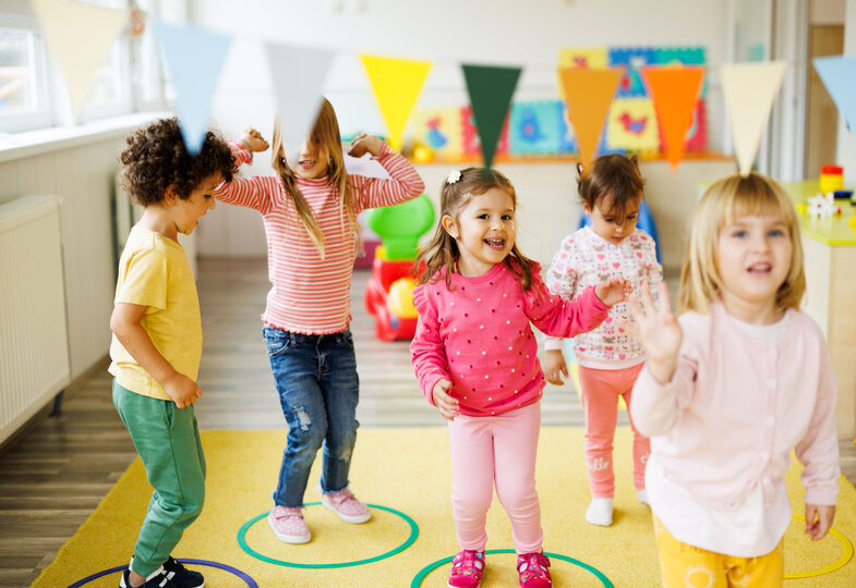 Fünf Kinder stehen in bunten Kreisen, lachen und tanzen fröhlich.
