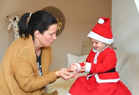 Ein Kind im Weihnachtskostüm sitzt einer Frau gegenüber, und beide heben die Hände einander entgegen.