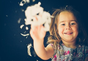 Ein Kind wirft lachend eine Handvoll weiße Federn in die Luft. 