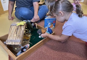 Ein Kind spielt mit gehäkelten Krippefiguren und der zugehörigen Weihnachtskrippe.