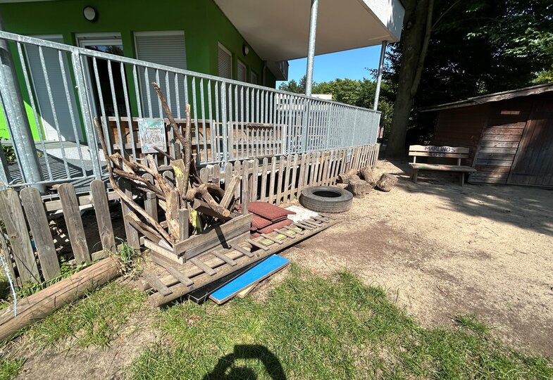 Ein grünes Haus mit einer eingezäunten Veranda und davor sind verschiedene Materialien, wie Reifen, Äste und Leitern. 