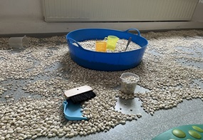 Eine große blaue Schale mit Bohnen steht in der Mitte, und darum herum liegen weitere Bohnen, Becher und Schaufeln.