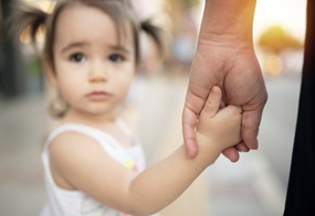 Ein kleines Mädchen blickt bedrückt in die Kamera, im Fokus liegt ihre Hand, die die einer erwachsenen Person hält.