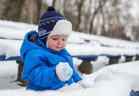 Ein Kind sitzt im Schnee und hält Schnee in der Hand.