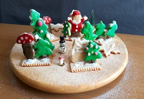 Aus Keksen ist ein kleines Winterwäldchen gestaltet, mit Tannenbäumen, einem Schneemann, Pilzen und einem Weihnachtsmann.