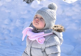 Mädchen steht im Schnee und schaut nach oben.