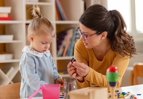 Eine Frau und ein Kleinkind spielen am Tisch mit Steckbauklötzchen. 
