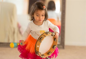 Kleines Mädchen spielt mit Tamburin und Rassel.