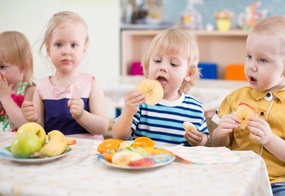 Die Kinder sitzen alle an einem Tisch und essen gemeinsam verschiedenes Obst.