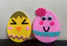 Filzstoff in Eierform, die mit lustigen Gesichtern beklebt sind.