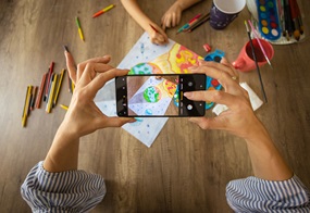 Ein gemaltes Bild von einer Weltkugel wird fotografiert mit einem Handy. 