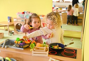 Zwei Kinder kochen konzentriert gemeinsam in einer Spielküche.