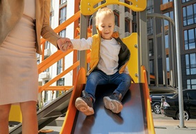 Ein kleiner Junge versucht eine Rutsche runter zu rutschen, an einer Hand wird er gehalten von einem Erwachsenen.