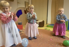 Drei Kinder stehen nebeneinander und tragen bunte Kleider oder Röcke.