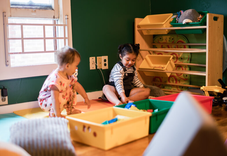 Zwei Kinder spielen miteinander und um sie herum sind viele Aufbewahrungsbehälter mit Spielzeug drin. 