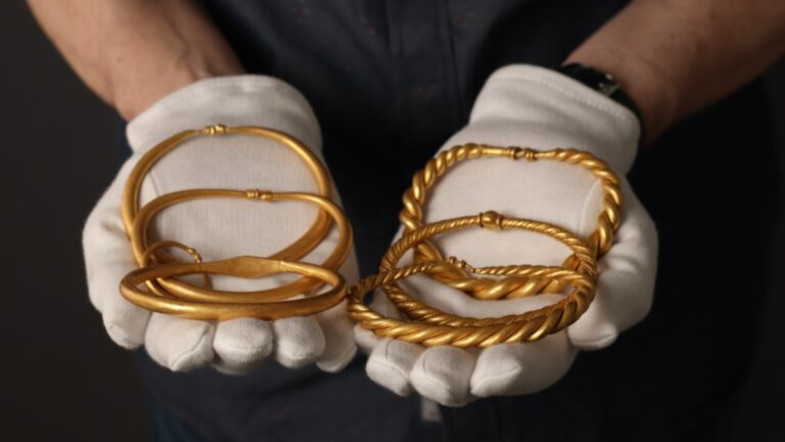 Goldene Wikingerarmreifen mit unterschiedlichen Mustern werden von einer Person mit weißen Handschuhen gehalten