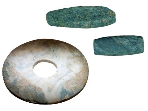 Drei grünlich-braune Steinobjekte, darunter eine runde Scheibe mit Loch und zwei längliche, abgeflachte Steine