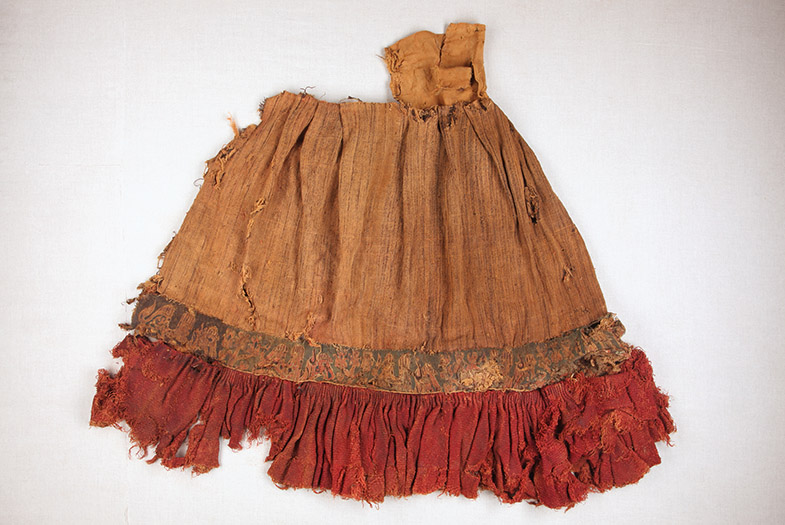 Altes, zerfleddertes Kleidungsstück mit Fransen und einem dekorativen Stoffband