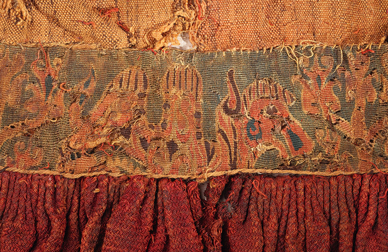 Nahaufnahme eines gewebten Stoffes mit figürlichen Mustern und Fransen am unteren Rand