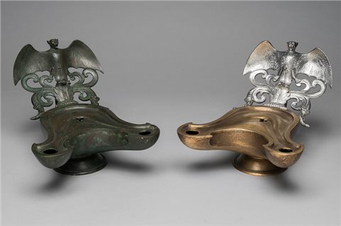Zu sehen sind zwei Öllampen mit jeweils zwei Öffnungen. Das Original aus Stabiae ist aus Bronze und dunkel verfärbt, während der Nachguss zweifarbig ist: Die Lampe ist kupferfarben und der Fledermausreflektor silbern. Die Fledermäuse sitzen auf stilisierten Ranken mit weit ausgebreiteten Flügeln.