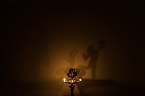 Lichttest mit einer Trilychnis. Bedingt durch die drei Flammen, wird der Schatten des Tänzers durch das Licht drei mal an die Wand geworfen. Der linke Schatten ist am größten und sehr verzerrt und undeutlich zu erkennen, während der mittlere Schatten deutlich zu erkennen ist. Der rechte Schatten ist größer als der mittlere und dunkler, seine Umrisse sind nur leicht verzerrt.