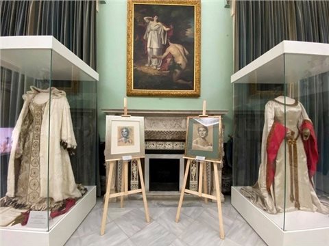 Blick in die Ausstellung. Zu sehen sind zwei Kostüme der Sängerin Maria Callas sowie zwei Porträts von ihr. Dahinter hängt an einer grünen Wand ein Bild von Nasikaa und Odysseus.