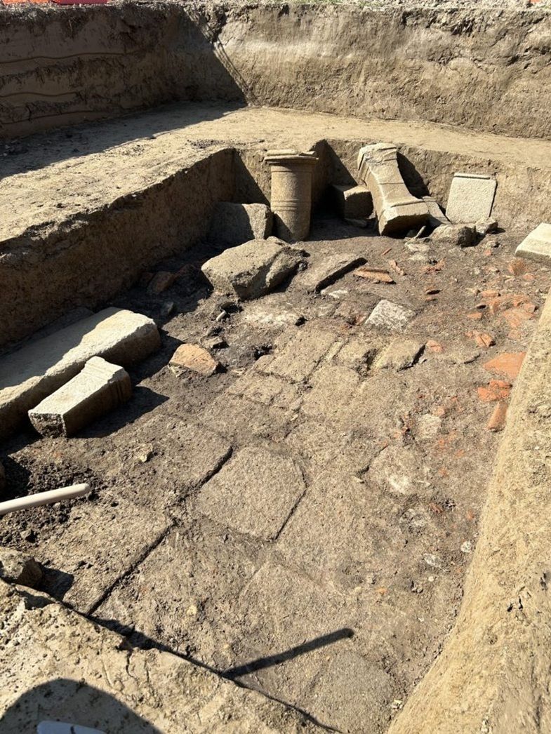 Freigelegter archäologischer Bereich mit antiken Säulenteilen und Steinplatten in einer Ausgrabungsstätte