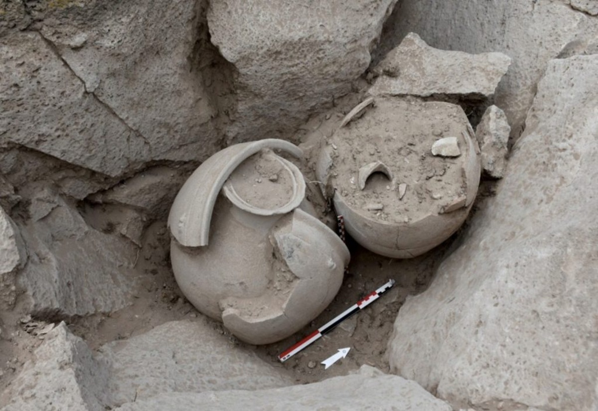 Zwei teilweise zerbrochene, antike Tongefäße liegen in einer Ausgrabungsstätte zwischen Steinen und Erde.
