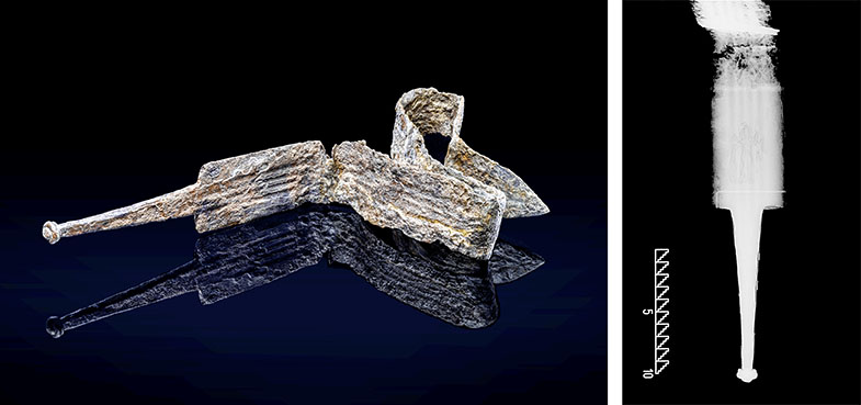 Im linken Bildbereich liegt ein stark korrodiertes, längliches Metallobjekt mit einer schmalen Spitze und einer gewundenen, bandartigen Struktur auf einer dunklen Oberfläche. Rechts daneben zeigt eine schwarz-weiße Röntgenaufnahme das Objekt in vertikaler Ausrichtung, wobei die innere Struktur und Materialdichte sichtbar werden. Am unteren Rand der Röntgenaufnahme befindet sich eine kleine, gestufte Skala.