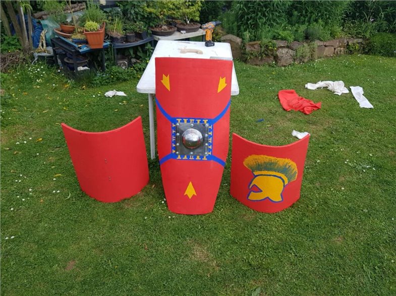 Links und rechts jeweils eine parmula, zentral das angeschrägte scutum. Die kleineren parmulae wurde vom Thraex („Thraker“) genutzt. Das scutum ist deutlich schwerer, bietet dafür jedoch erhöhten Schutz.