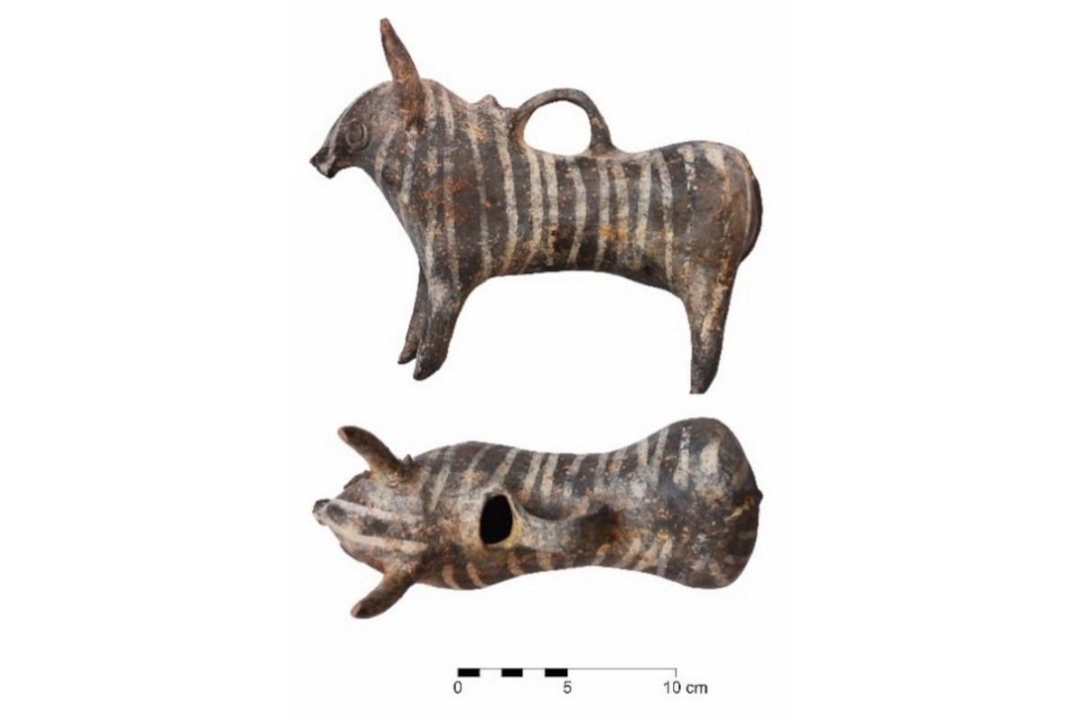 Zwei Ansichten eines kleinen, länglichen Keramikgefäßes in Form eines stilisierten Tieres mit Hörnern und einem Henkel auf dem Rücken. Die Oberfläche zeigt ein Muster aus hellen und dunklen Streifen. Unterhalb der Abbildungen befindet sich eine Maßstabsleiste mit einer Einteilung von 0 bis 10 cm.