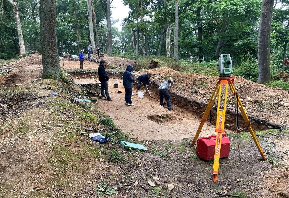 Mehrere Archäologen arbeiten auf der Ausgrabungsstätte am Kapellenberg im Wald. Im Vordergrund steht ein Vermessungsinstrument