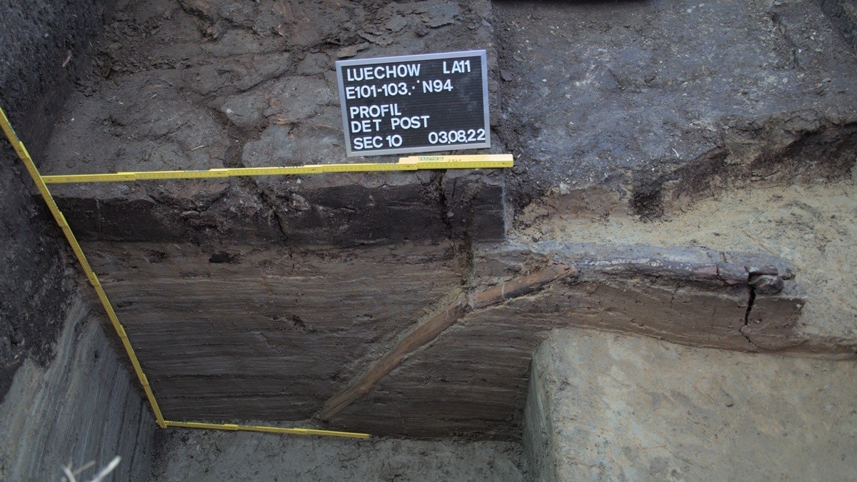 Ausgegrabener Erdquerschnitt mit sichtbaren Bodenschichten und Messlatten an den Seiten