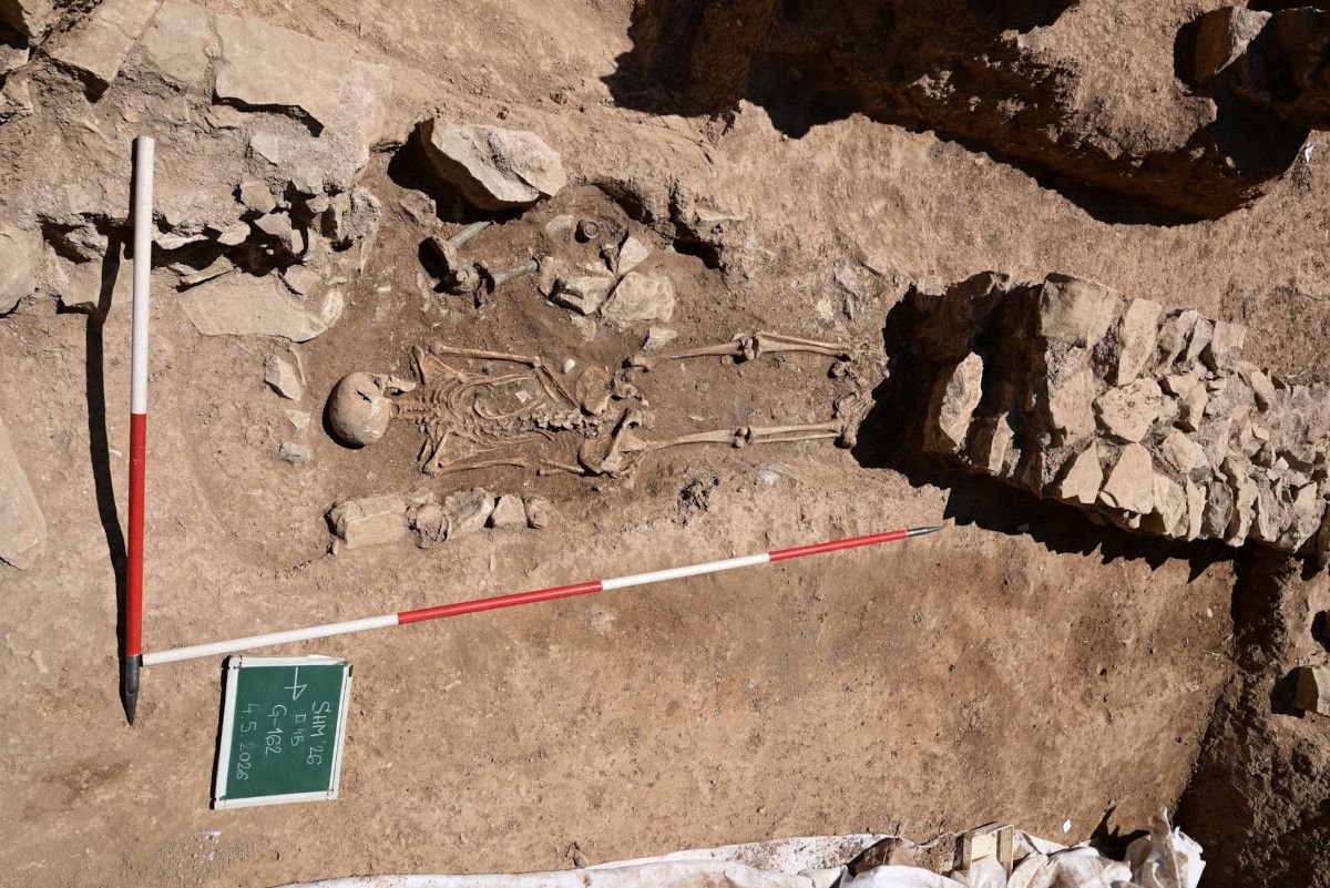 Skelett in Bauchlage in einer archäologischen Ausgrabungsstätte mit mehreren Beigaben und Messstäben