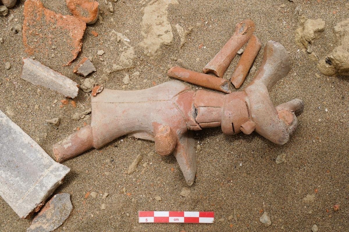Terrakottafigur eines Krieger liegt umgeben von Scherben im Sand. Davor ein Maßstab