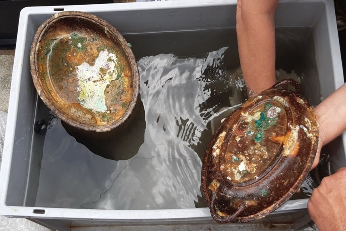 Zwei Teile eines Serviertablettes mit Patina und Ablagerungen vom Meer liegen in einem Behälter mit Flüssigkeit an Bord des Bergungsschiffes