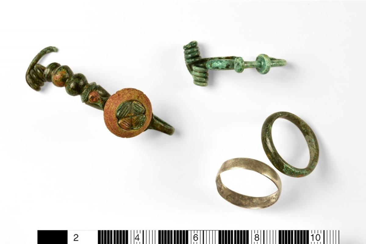 Funde aus mehreren Bestattungen nach ihrer Restaurierung: bronzene Fibel mit Korallenzier, bronzene Fußzierfibel, jeweils ein Fingerring aus Silber und aus Bronze