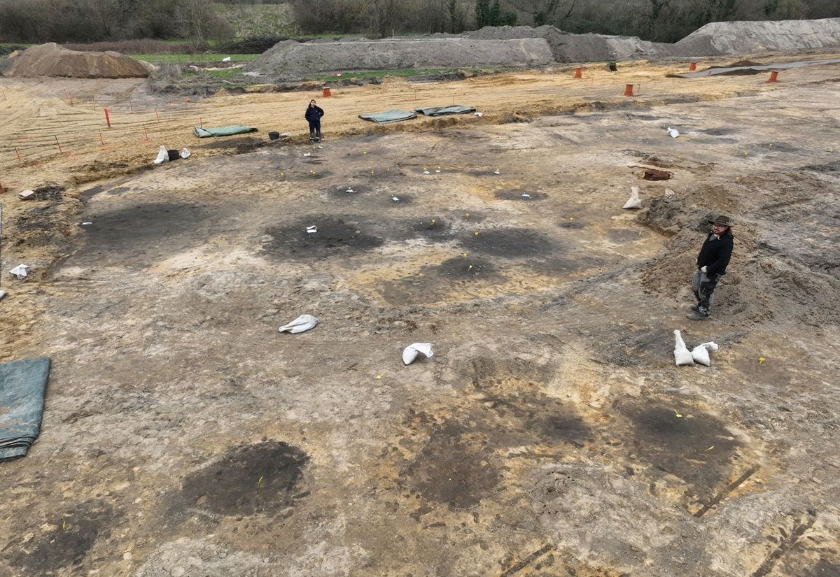 Viele Pfostengruben und ein großer Brunnenschacht (hinten links) zeichnen sich im hellen Sand als schwarze Verfärbungen gut ab.