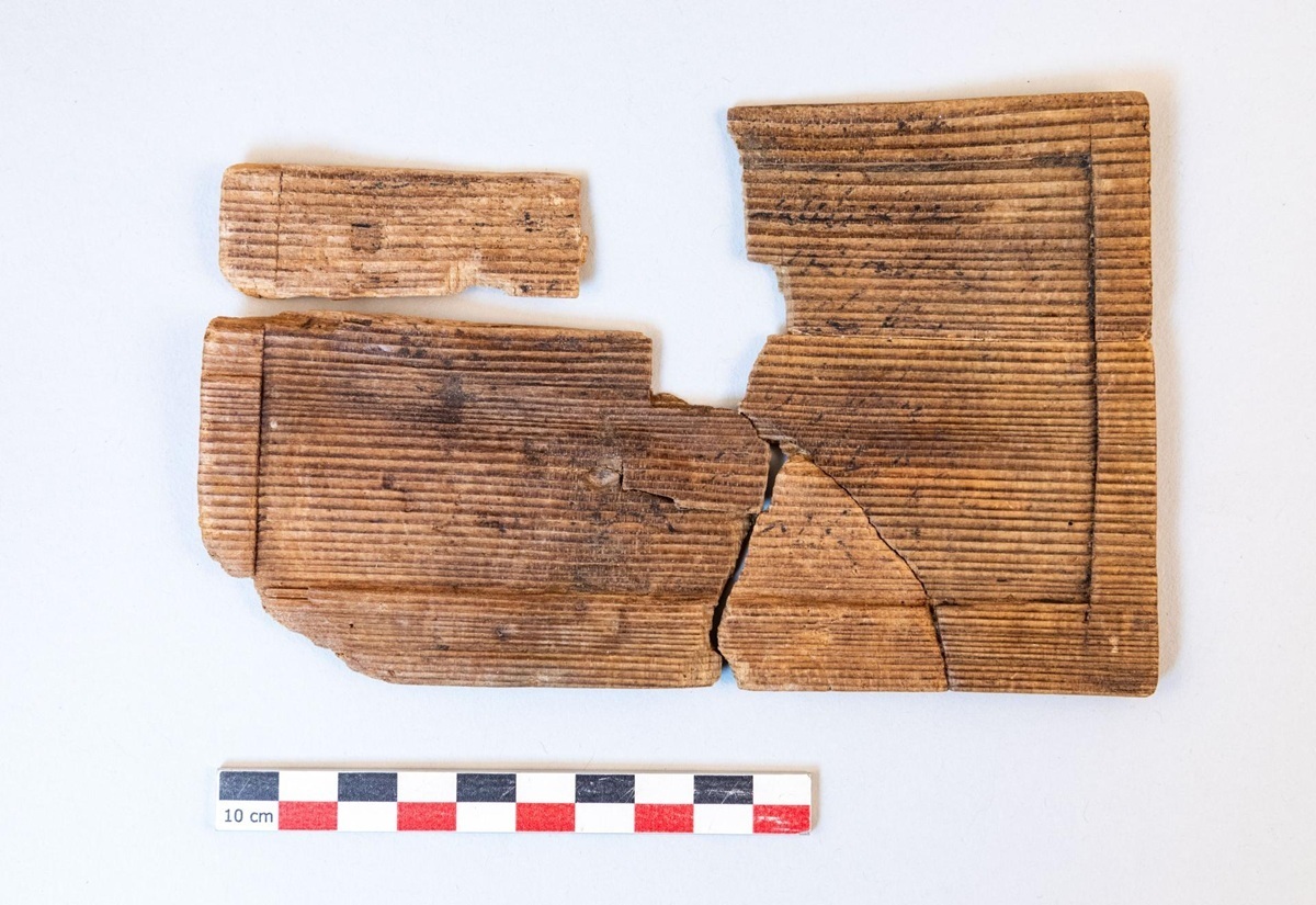 Zerbrochene, rechteckige Holzplatte mit Rillenmuster und Messskala darunter.