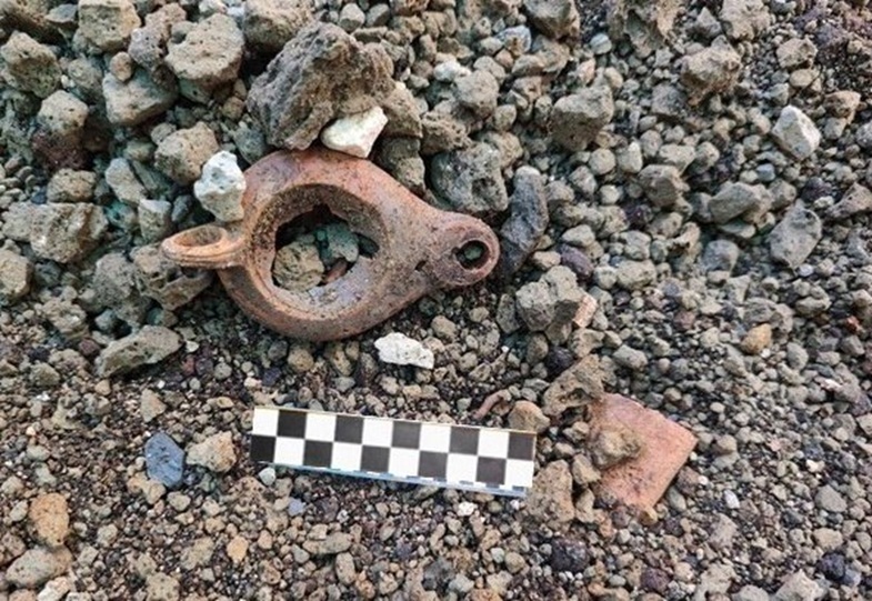 Archäologischer Fund eines zerbrochenen antiken Öllampenkörpers aus Ton auf vulkanischem Gestein mit Maßstabslineal