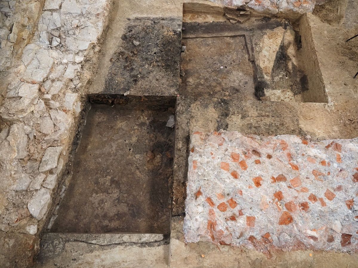 Archäologische Ausgrabung mit zwei rechteckigen Grabungsschnitten im Boden, in denen sich Steinfundamente befinden