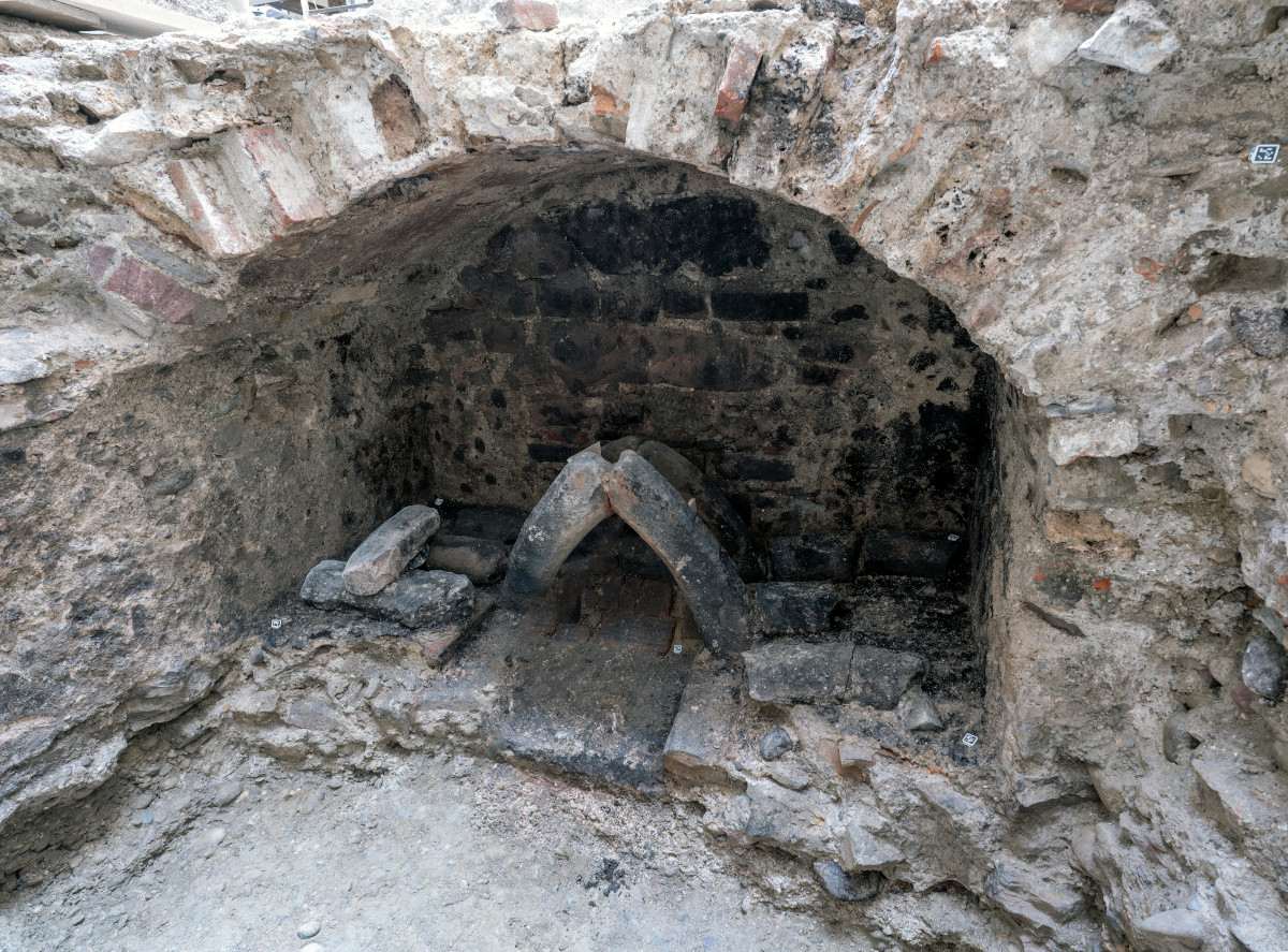 Gewölbte Steinstruktur mit einer Öffnung, die von grob behauenen Steinen eingefasst ist. Im Inneren sind zwei steinerne Bögen sichtbar, die auf dem Boden aufliegen und von weiteren Steinen flankiert werden. Die Wand und der Boden bestehen aus unregelmäßigem Mauerwerk, das Spuren von Alter und Abnutzung zeigt.