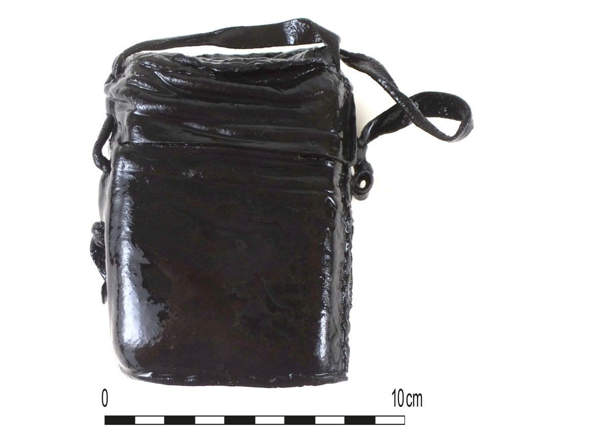 Kleiner, rechteckiger, schwarzer Ledereinband mit Schlaufe und sichtbaren Nähten, daneben Maßstab bis 10 Zentimeter